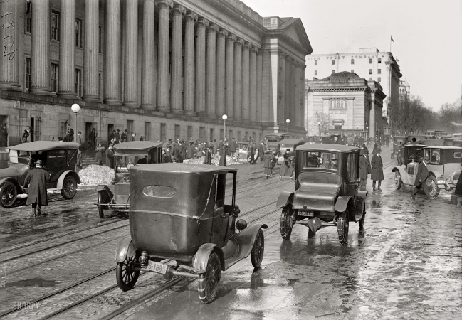 Photo showing: Fifteenth Street: 1918 -- Washington, D.C. Motoring past the Treasury Building with chains on.