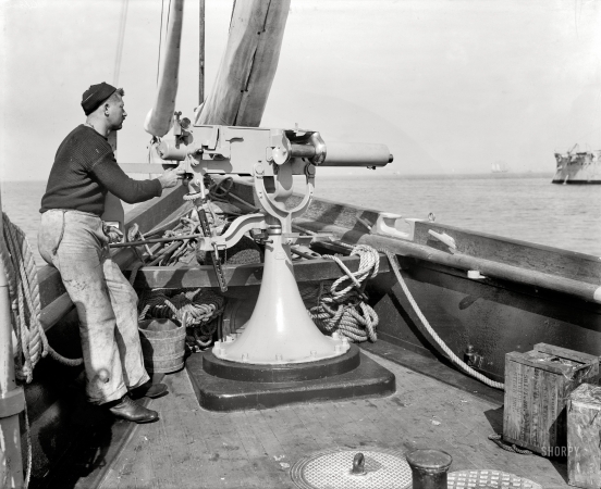 Photo showing: Fire Power -- U.S.S. Vixen, Maxim machine gun and gunner Smith, circa 1900.