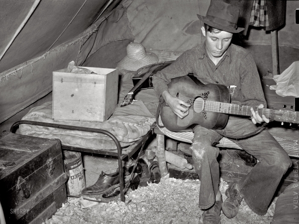Photo showing: Picker Picking -- April 1939. Migrant strawberry picker playing guitar in his tent near Hammond, Louisiana.