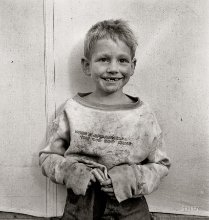 Photo showing: The Happy Camper -- November 1938, Shafter Camp, California. Migrant cotton picker's child who lives in a tent in the government camp.