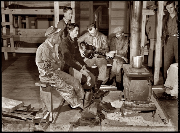 Photo showing: Bunkhouse Boys -- December 1940. Construction workers gathered around the bunkhouse stove
in the new craftsmen's barracks at Camp Blanding, Florida.