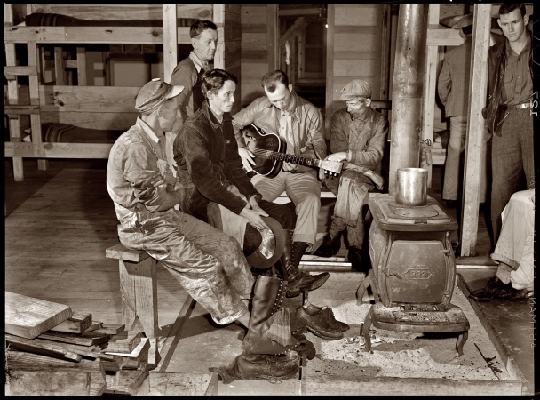 Photo showing: Bunkhouse Boys -- December 1940. Construction workers gathered around the bunkhouse stove
in the new craftsmen's barracks at Camp Blanding, Florida.