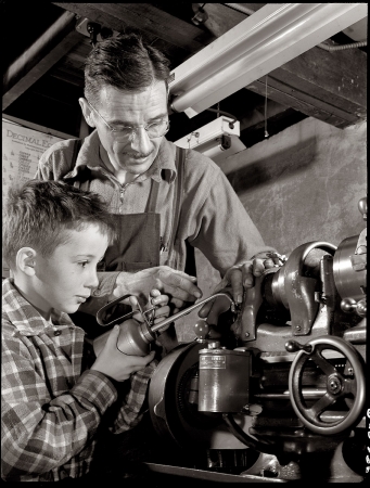 Photo showing: A Little Squirt -- 1942. George Carrell Jr. likes to watch his father produce essential war equipment in his Passaic home workshop.