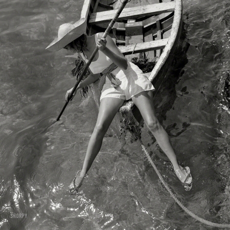 Photo showing: Fashionably Splayed -- 1938. Swimwear model on bow of skiff.