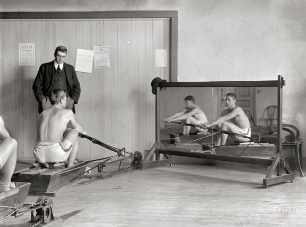 Photo showing: Crew Squad and Coach Rice -- February 1910. New York. Columbia rowing team in
mock shells training in crew house with coach Jim Rice.
