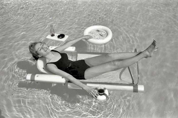 Photo showing: Flotilla -- April 1961. Sunbathing with the latest swimming pool equipment, including
a lounge chair with floating beverage holders and game table attachments.