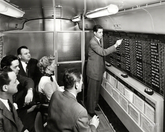 Photo showing: Inside Information -- 1954. Merrill Lynch account executive chalks up current
stock prices on quotation board in firm's new mobile office.