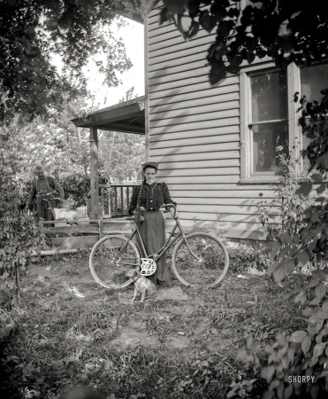 Photo showing: Miss Handlebars -- Circa 1900. Lettis -- girl with bicycle and dog.