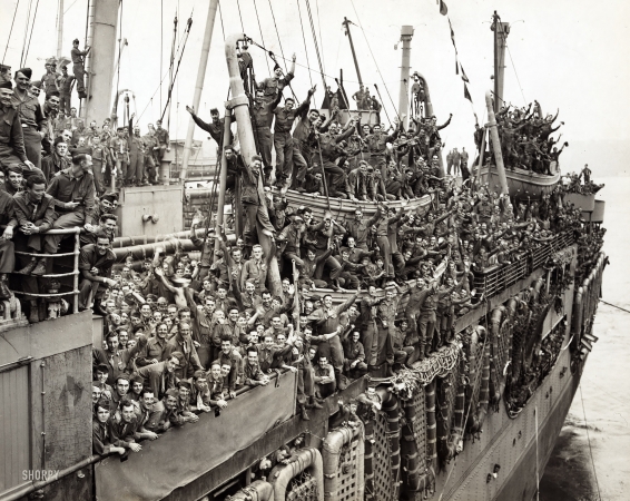 Photo showing: Home Again -- August 6, 1945. Troops of the 20th Armored Division and units of the 9th Army
whoop it up between raindrops as the S.S. John Ericsson nears Pier 84, Hudson River.