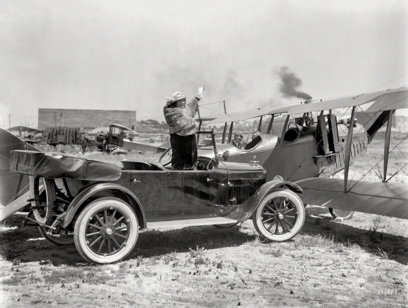 Photo showing: Flapper Up -- San Francisco circa 1920. Studebaker touring car with biplane at airfield.