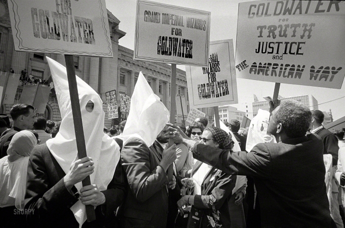 Photo showing: Wizards for Goldwater -- July 12, 1964. Ku Klux Klan members supporting Barry Goldwater's campaign for the presidential nomination
at the Republican National Convention, San Francisco, as an African American man pushes signs back.
