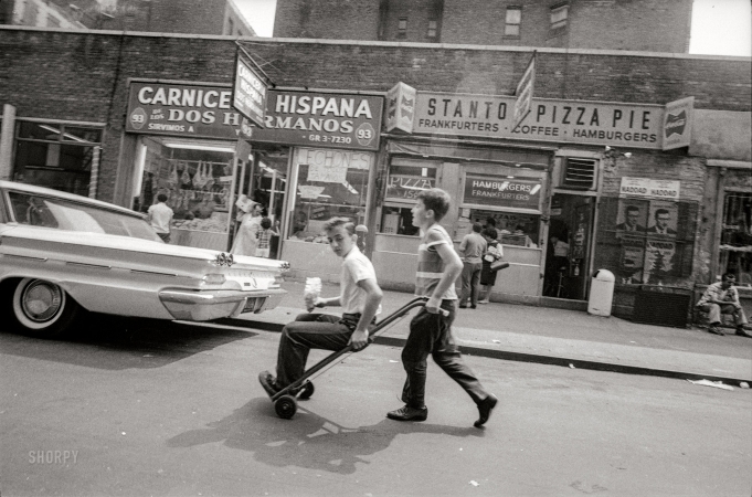 Photo showing: Dos Hermanos -- July 1964. New York. Two boys in street, one riding inside hand truck.