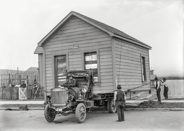Photo showing: House Movers -- San Francisco circa 1919. Truck moving house. Note the soapbox racer on roller-skate wheels.