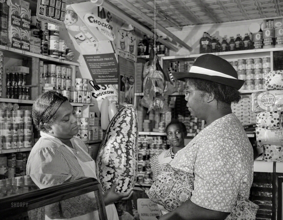 Photo showing: An Impressive Specimen -- August 1942. Washington, D.C. Housewife bargaining in the store owned by Mr. J. Benjamin.