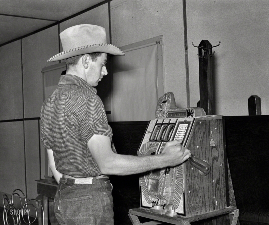 Photo showing: All Hat -- June 1939. Birney, Montana. Dude playing a slot machine.