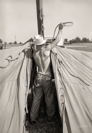 Photo showing: Back at Work -- May 1938. Member of carnival crew at work erecting tent
for Lasses White traveling show. Sikeston, Missouri.