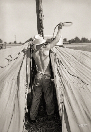 Photo showing: Back at Work -- May 1938. Member of carnival crew at work erecting tent
for Lasses White traveling show. Sikeston, Missouri.