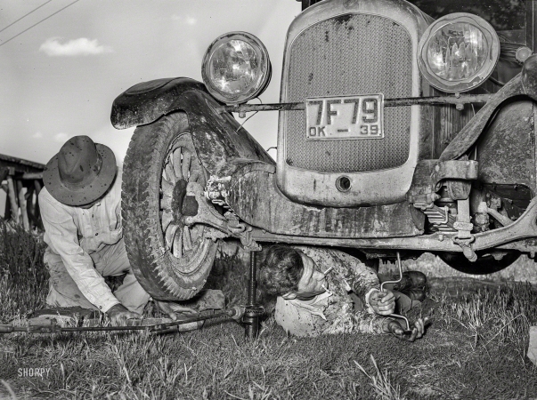 Photo showing: A Tight Spot -- June 1939. Migrant steeplejack removing the crankcase from his automobile near Prague, Oklahoma.