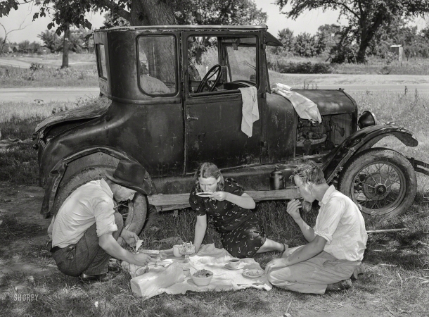 Photo showing: T for Three -- June 1939. Migrant workers eating dinner by the side of their car while they are camped near Prague, Lincoln County, Oklahoma.