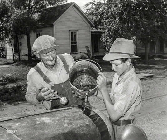 Photo showing: Check Coolant -- July 1939. En route to California. Pouring water into radiator of migrants' car in the streets of Muskogee, Oklahoma.