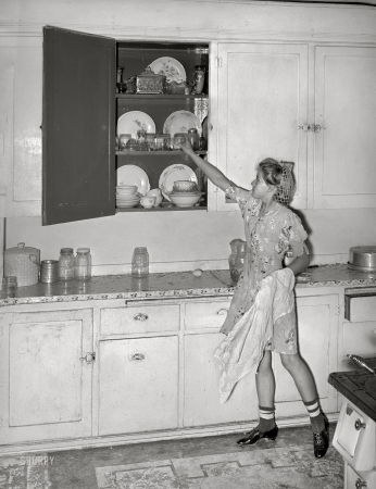 Photo showing: Pride of Plates -- August 1940. Daughter of Mormon farmer putting away dishes in kitchen cabinet. Box Elder County, Utah.