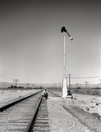 Photo showing: Career Track. -- February 1939. Looking east down the railroad track near
Calipatria. Single men, itinerants with 'bindles,' waiting for the freight.