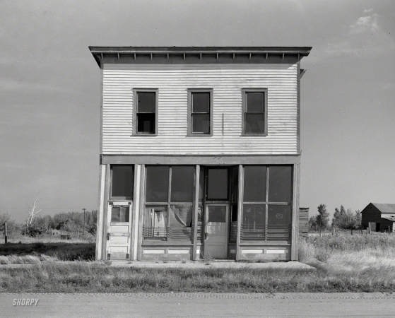 Photo showing: Leaning Out -- August 1937. Abandoned store building on what was the main street. Gemmel, Minnesota.