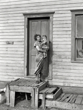 Photo showing: Cam Ham -- November 1937. Mrs. John Baker and baby on steps of farm home. Divide County, North Dakota.