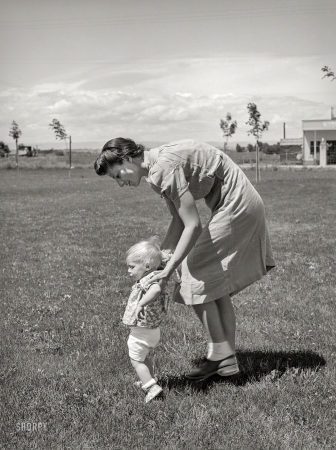 Photo showing: Baby Steps -- June 1941. Farm worker's wife teaches her baby girl to walk at the FSA labor camp. Caldwell, Idaho.