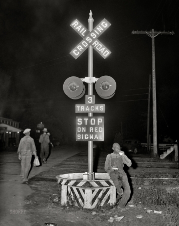 Photo showing: Sign of the Cross. -- July 1940. Migratory agricultural worker has his supper (a nickel pie
and a glass of milk) at the railroad crossing at Camden, North Carolina.