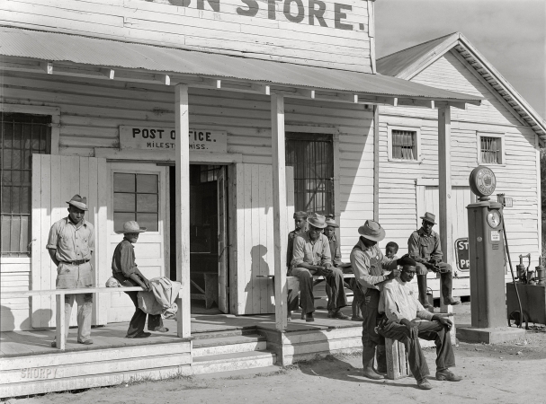 Photo showing: All the Trimmings. -- November 1939. Negroes cut each other's hair in front of plantation store<br  />
after being paid off on Saturday. Mileston Plantation, Mississippi Delta.