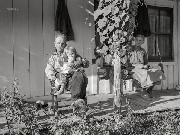 Photo showing: Baby Doll. -- September 1940. Mountaineer with neighbor and her grandchildren
on front porch of their home up Frozen Creek. Breathitt County, Kentucky.