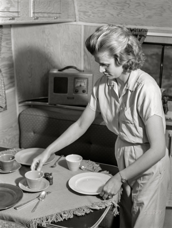 Photo showing: Home Plate -- June 1941. Wife of defense worker setting table for
dinner in trailer home. Trailer camp at Erie, Pennsylvania.