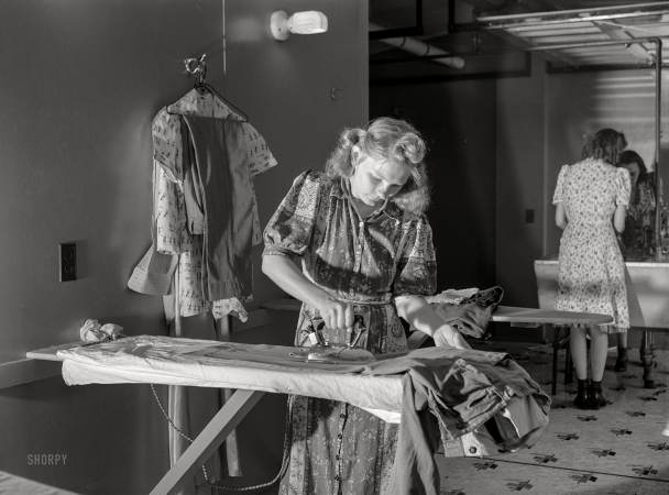 Photo showing: Ironed Out -- June 1941. Wife of defense worker ironing clothes in utility building at FSA trailer camp. Erie, Pennsylvania.