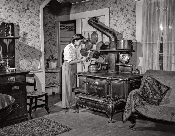 Photo showing: Russian Style! -- August 1942. Hartford, Connecticut (vicinity). Mrs. Boris Komorosky in
her living room. Stove is for heat in winter, Russian style! Photo by John Collier. 