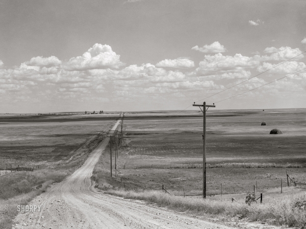 Photo showing: The Lonesome Road -- August 1941. Road with Homestead, Montana, and grain elevators on the horizon.