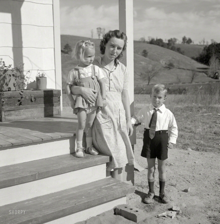 Photo showing: The Howard Smiths -- October 1941. Radford, Virginia (vicinity). Elsie Marie and Howard Jr., children of
Mr. Howard H. Smith, with their mother on the porch of their new rural home.