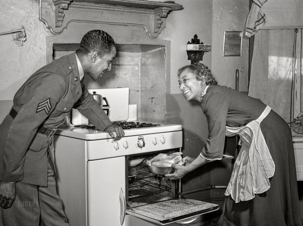 Photo showing: Chicken Dinner! -- March 1942. Baltimore, Maryland. Sergeant Franklin Williams, home on leave
from Army duty, watching his mother put chicken into the oven.