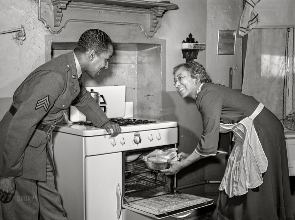 Photo showing: Chicken Dinner! -- March 1942. Baltimore, Maryland. Sergeant Franklin Williams, home on leave
from Army duty, watching his mother put chicken into the oven.