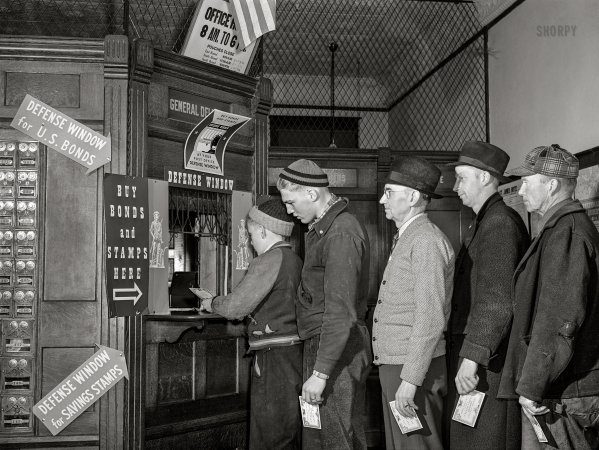 Photo showing: Defense Window -- April 1942. Postmaster in a small Minnesota town selling defense bonds to Swedish farmers.