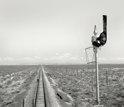 Photo showing: Backtrack -- March 1943. Willard, New Mexico. Santa Fe flagman walks back to signal
any oncoming trains during a stop for water between Vaughn and Belen.
