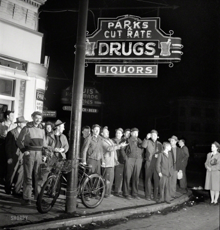 Photo showing: Flash Mob -- April 1943. Baltimore, Maryland. Third shift workers waiting
on a street corner to be picked up by car pools around midnight.