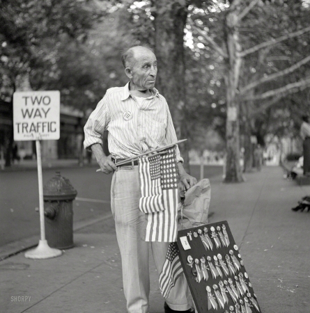 Photo showing: Vendor No. 113 -- July 1943. Washington, D.C. A man selling flags and buttons at the parade to recruit civilian defense volunteers.