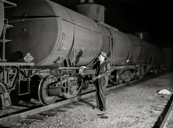 Photo showing: Yard Cop -- October 1942. Tulsa, Oklahoma. Mid-Continent Petroleum refinery.
Armed railroad guard inspecting an oil tank car in the yards.