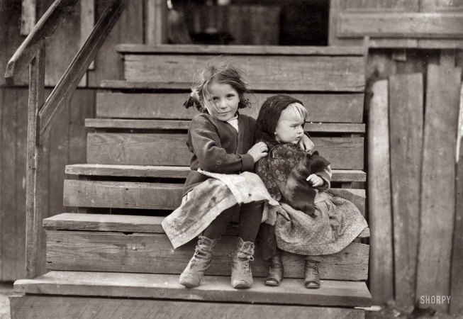 Photo showing: Step Sisters -- February 1911. Bayou La Batre, Alabama. Little Julia tending the baby at home.
All the older ones are at the factory. She shucks [oysters] also. Alabama Canning Co. 
