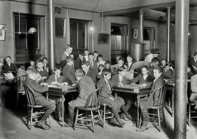 Photo showing: Newsboys Club -- October 1909. Boston, Mass. In the Newsboys Reading Room. Boys seated at tables playing games.