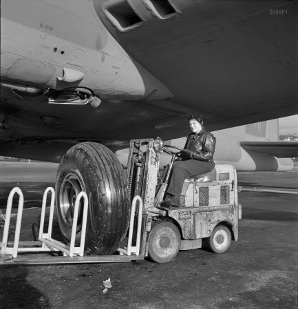 Photo showing: New Shoe -- December 1942. A landing wheel, with its huge rubber 'shoe,' is trundled out in a service tractor
to a new B-17F (Flying Fortress) bomber awaiting completion at Boeing's Seattle plant.