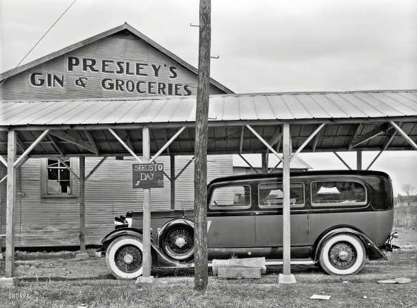Photo showing: Seedsto Day -- January 1939. Funeral ambulance parked under gin shed. Mound Bayou, Mississippi.