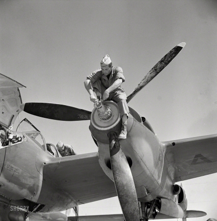 Photo showing: Now for the Tricky Part -- May 1942. Working on the nose of an engine on an interceptor plane. Lake Muroc, California.