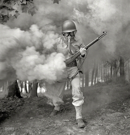Photo showing: Smokescream -- September 1942. Fort Belvoir, Virginia. Sergeant George Camblair
learning how to use a gas mask in a practice smokescreen.